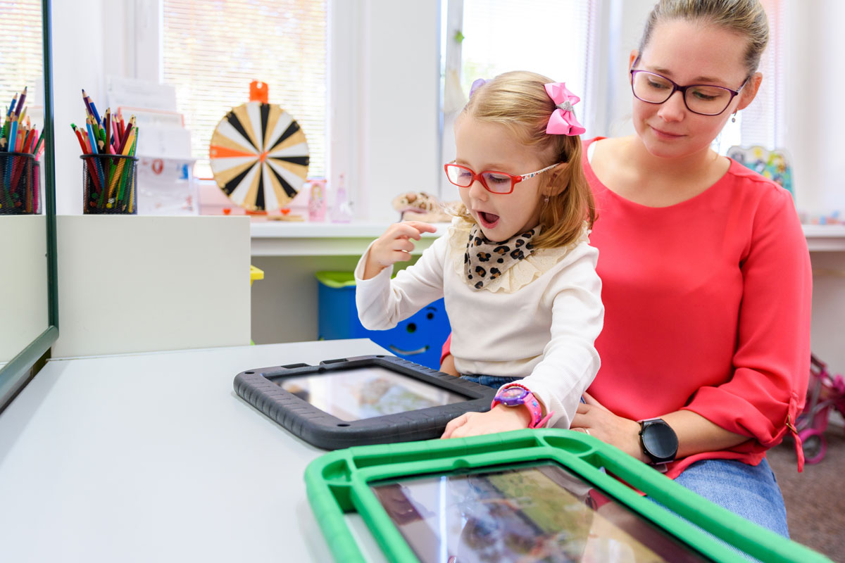 Girl using an AAC tablet with her speech therapist in El Paso