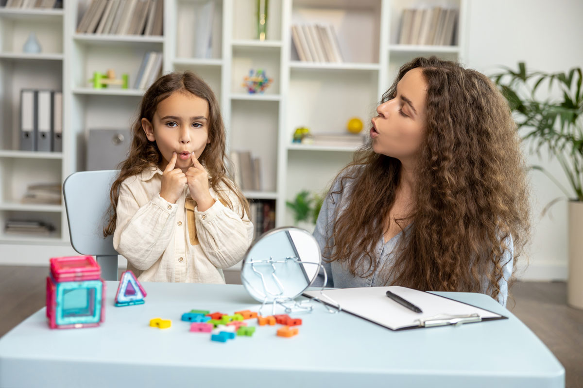 pediatric-speech-therapy-el-paso-mirror-practice-2 Speech therapist and girl practicing sounds with a mirror during pediatric speech therapy in El Paso
